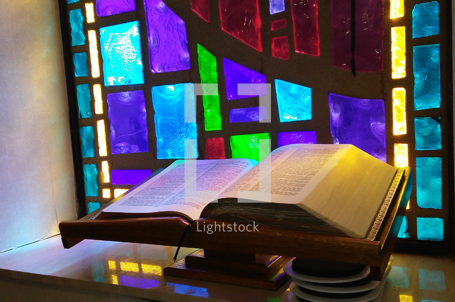 The Living Word of God open to the scripture passages in front of a stained glass window surrounded by sunlight and reflecting light prism ready to be read and alive and powerful for all those who hear and head the word of God. 