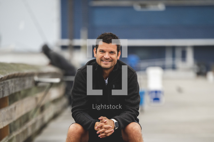 smiling man sitting on a pier 