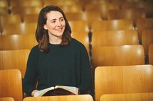 a woman reading a Bible alone in a church smiling 