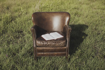 A Bible in a leather chair outdoors in a field at sunrise 