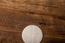A single communion wafer on a wooden surface.