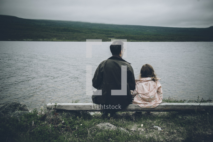 father and daughter sitting on a bench looking out at a lake 