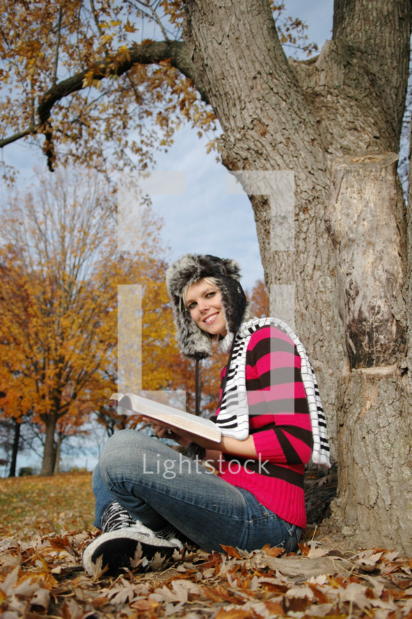 teen girl reading a Bible under a tree 