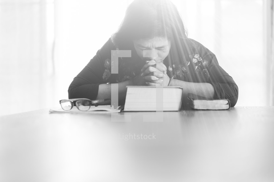 a woman sitting praying over a Bible 