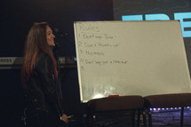 a worship leader standing on stage in front of a whiteboard with random rules listed 