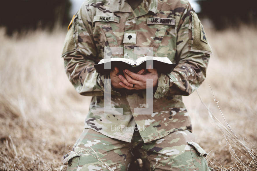 soldier kneeling reading a Bible in a field 