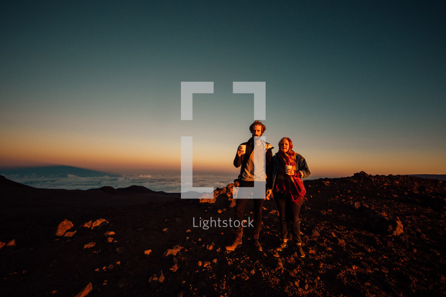 a couple holding hands standing on a mountaintop at sunrise 