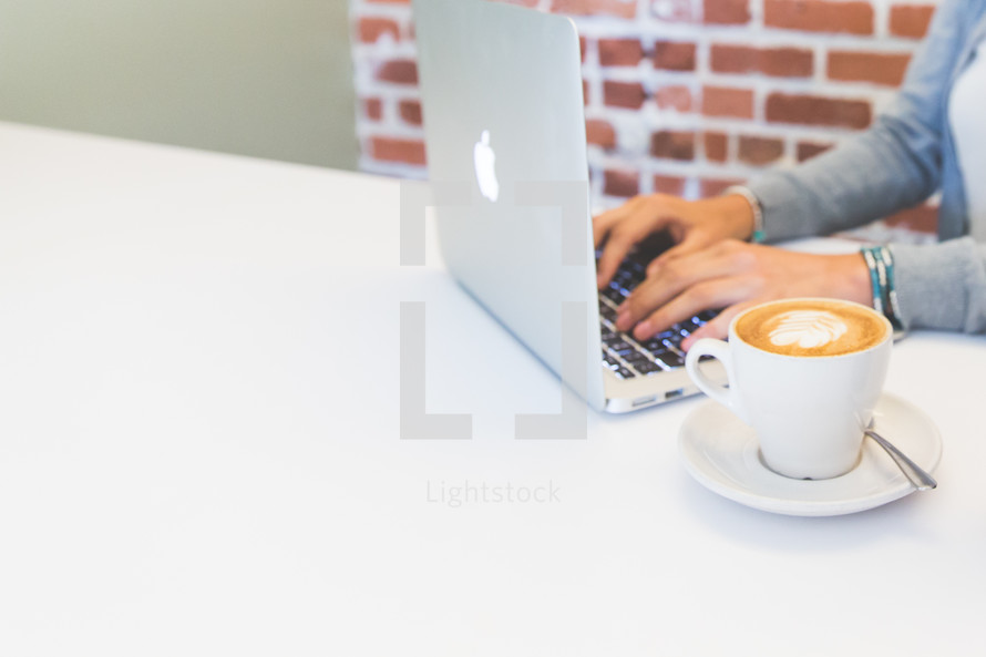 woman typing on a laptop next to a latte 