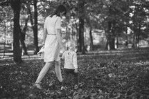 a mother and toddler daughter walking through fall leaves 