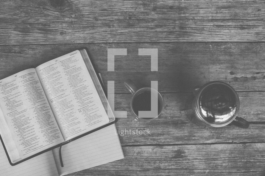 An open Bible and notebook next to a coffee mug and french press