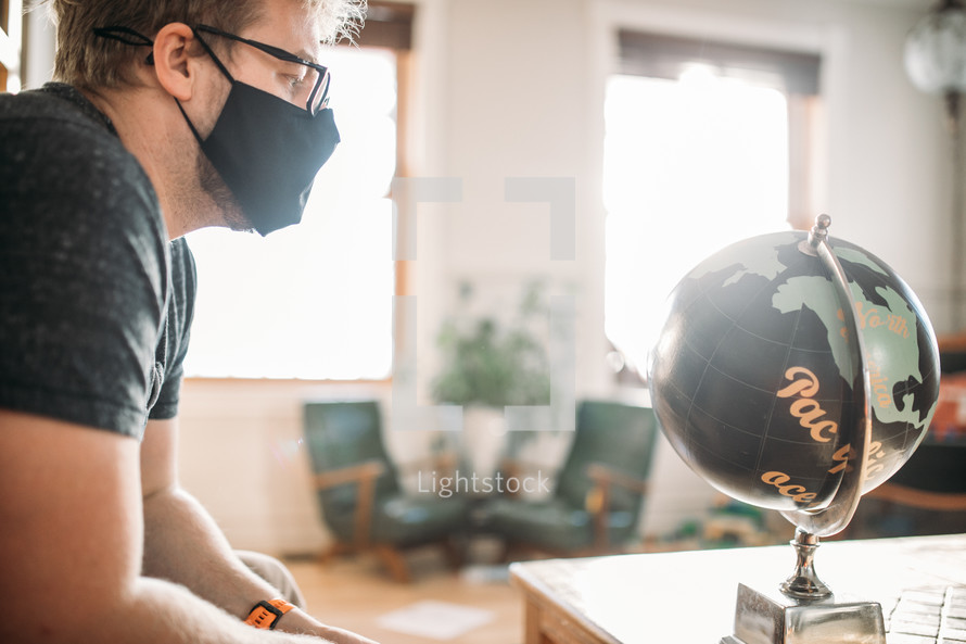 A man in a face mask looking at a globe  