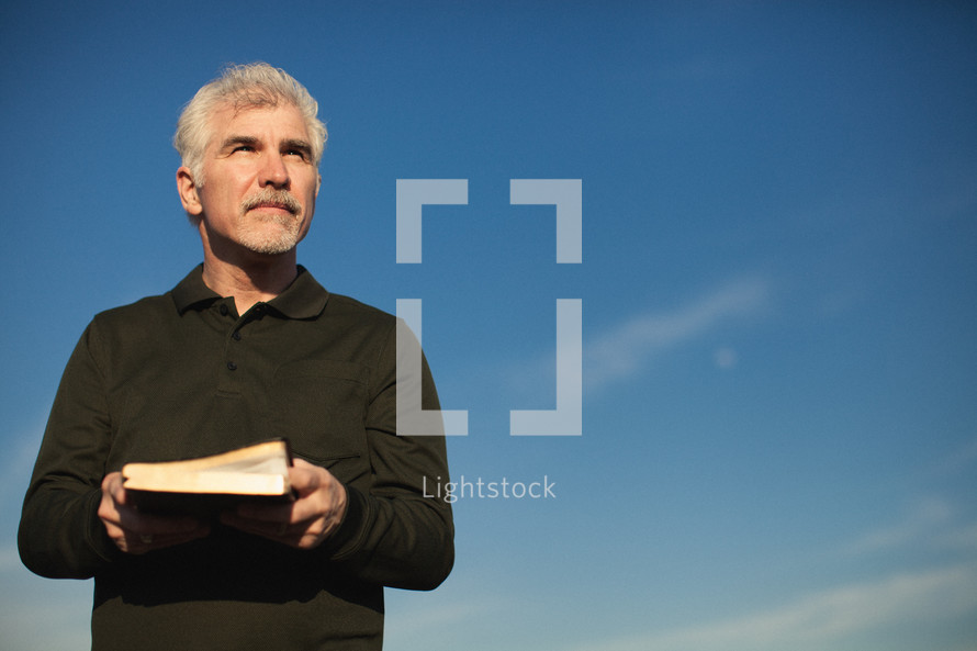 elderly man standing outdoors holding a Bible