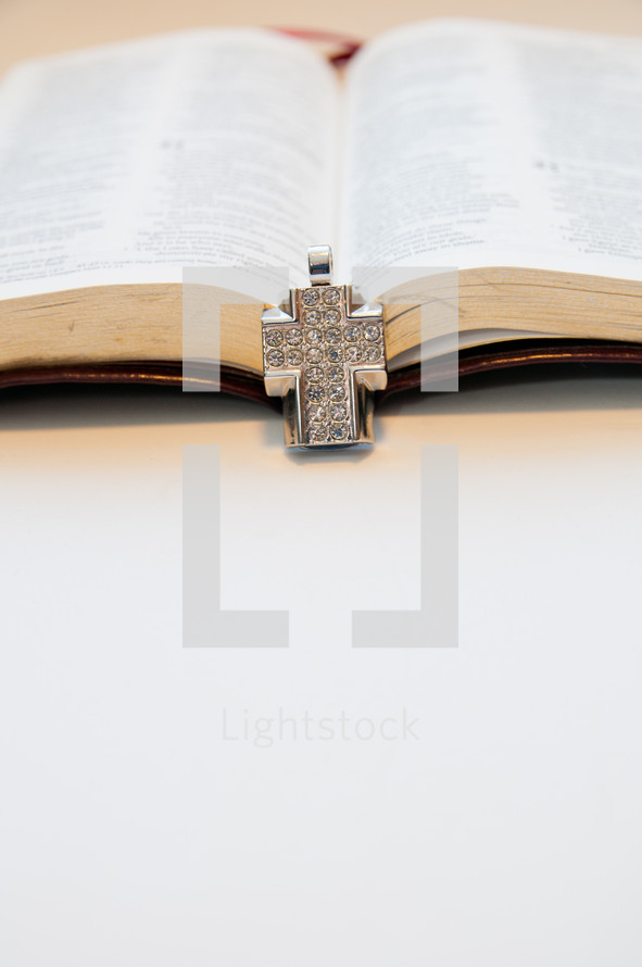 diamond studded cross necklace lying on the pages of a Bible