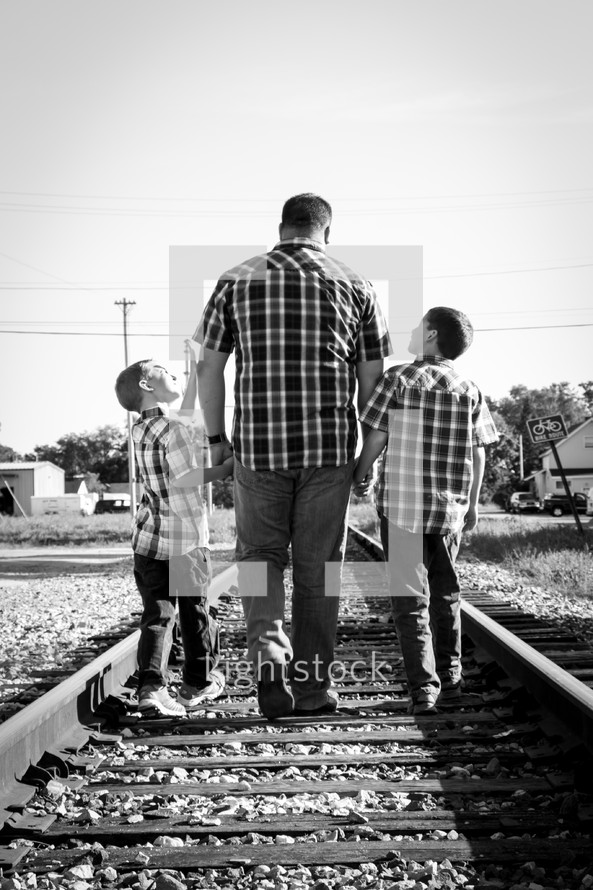 father walking holding hands with his sons on railroad tracks 