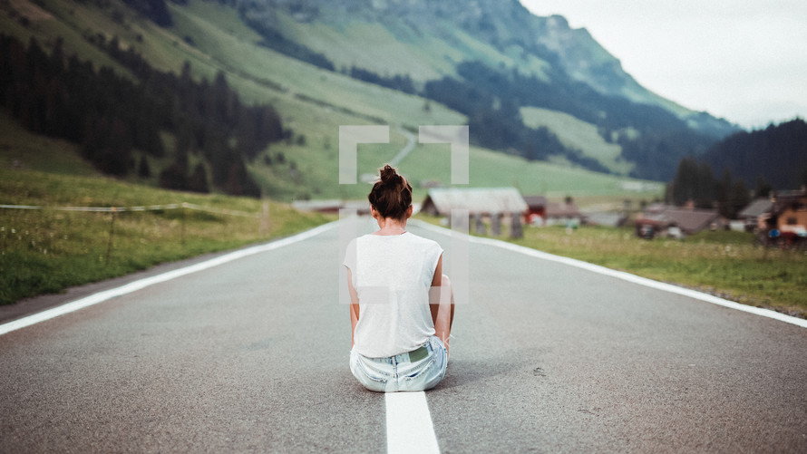 a young woman sitting in the middle of a rural street