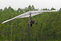 Hang glider in flight above a forest
