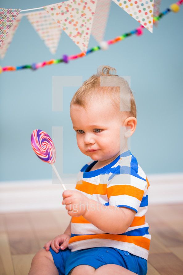 an infant boy holding a lollipop under a banner 