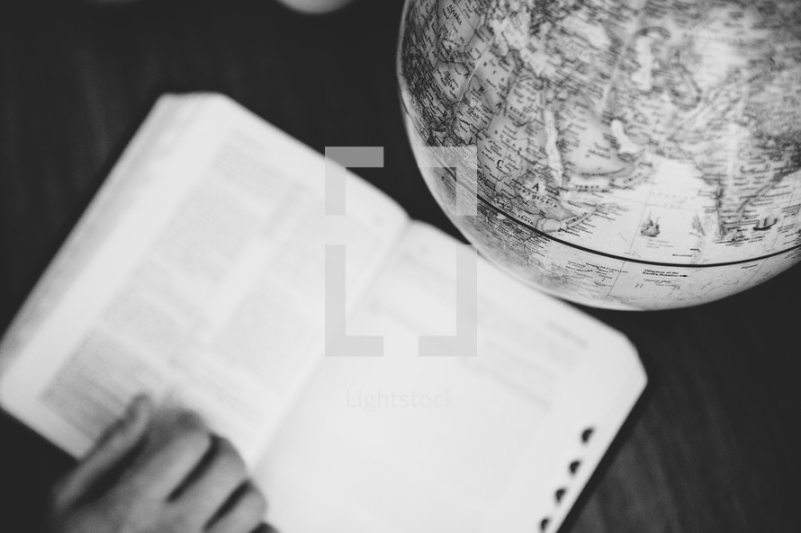 Someone reading a Bible next to a world globe.