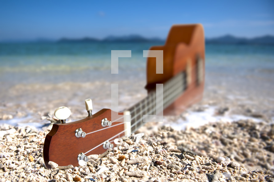 Guitar in the sand on the beach by the ocean.