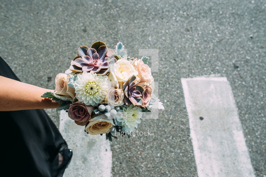 A floral bouquet held by a woman in a parking lot.