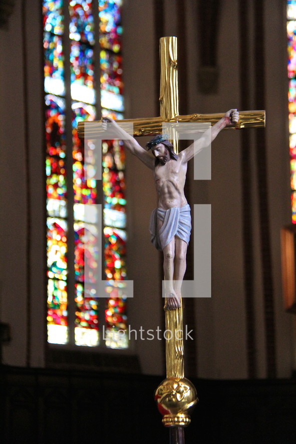 Golden catholic crucifix with stained glass cathedral windows behind