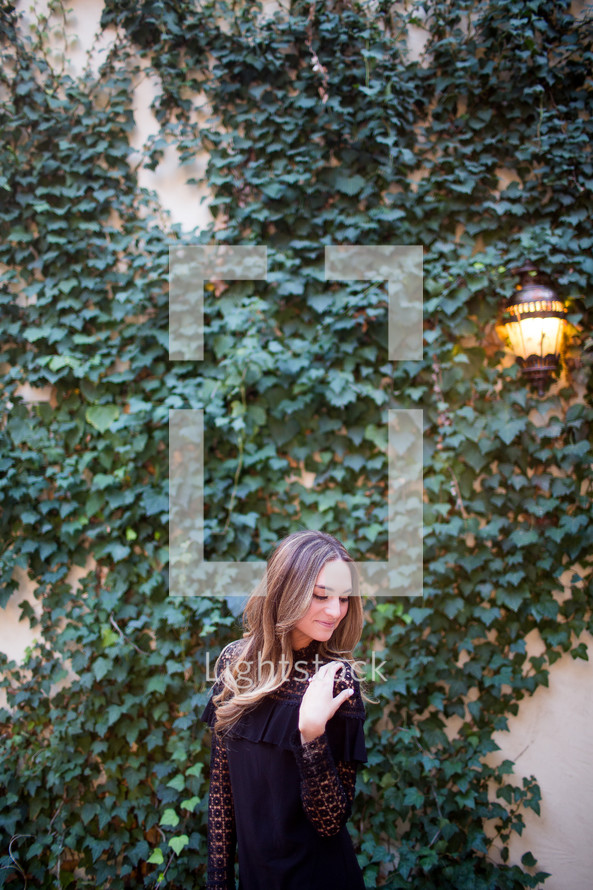 a woman posing in front of an ivy covered wall 