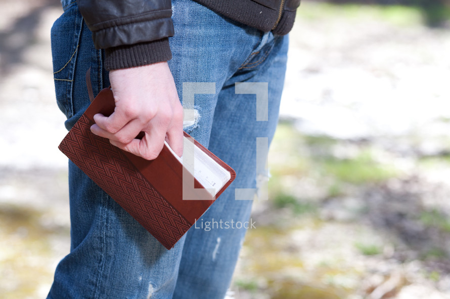 Man in jeans holding a Bible while standing outdoors.