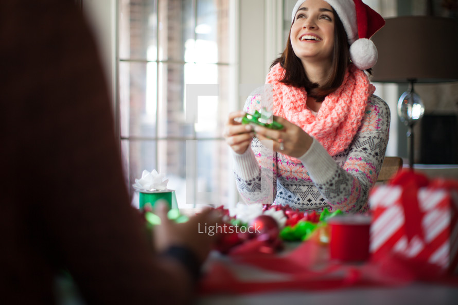 A young woman in a santa hat wrapping Christmas presents and laughing