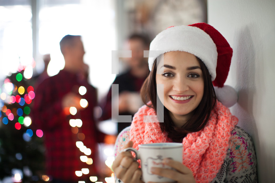 A smiling woman wearing a santa hat and holding a cup of coffee