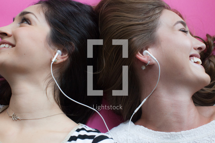 Two young women smiling and listening to music with ear phones.