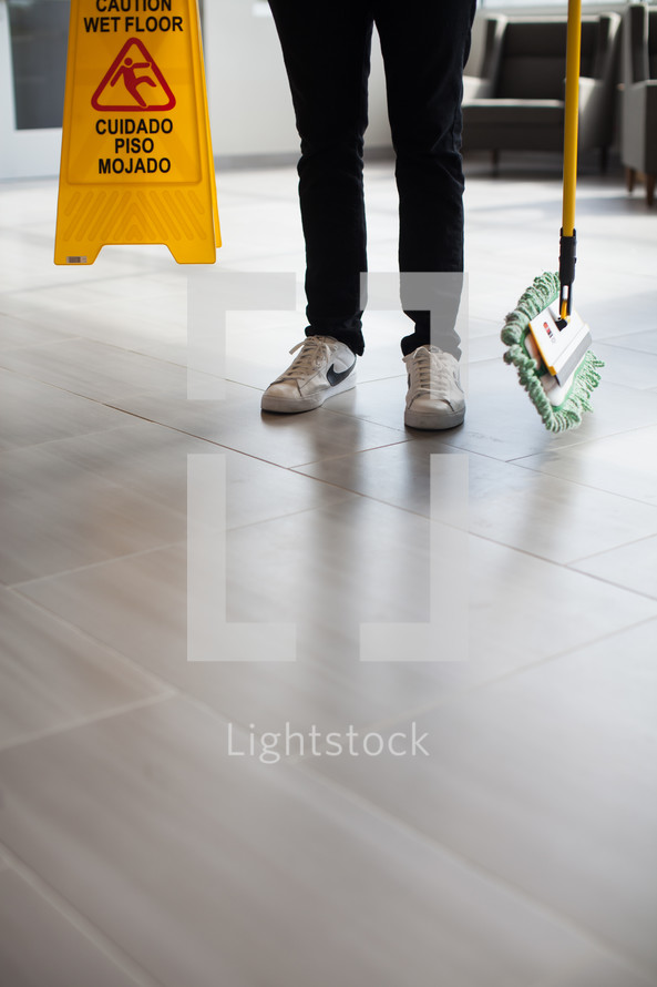 a man with a dust mop and a wet floor sign 