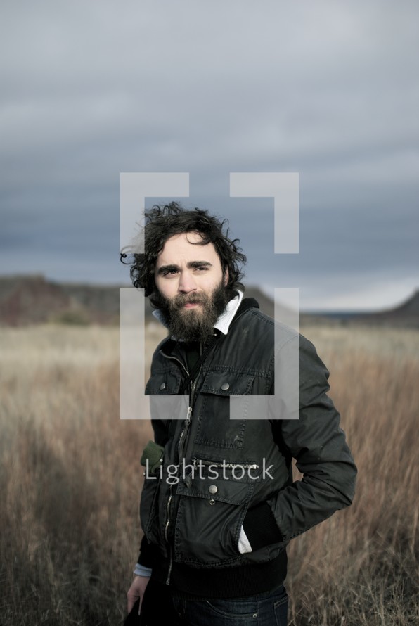 man with a beard standing alone in a field 