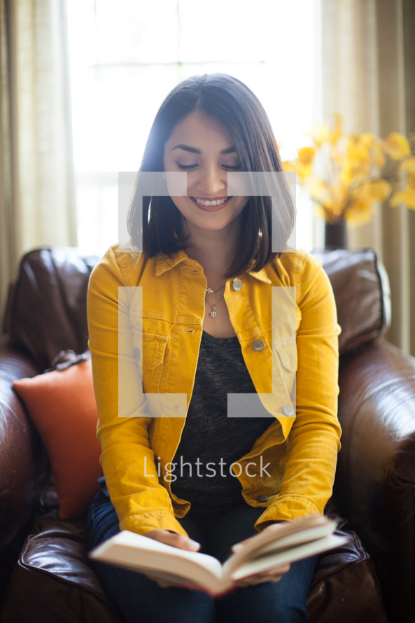a Latino woman sitting on a couch reading a Bible 