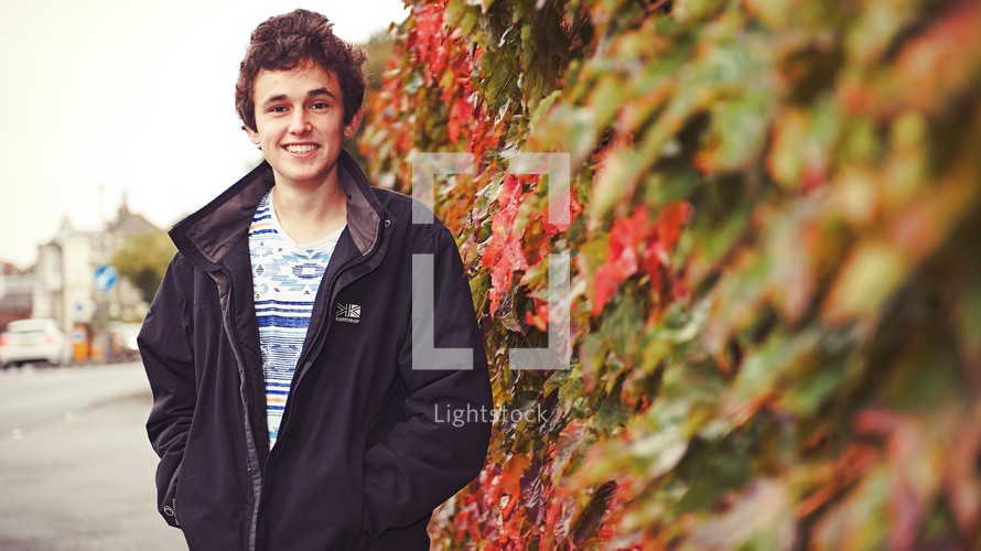 portrait of a teen boy standing near a wall covered in ivy