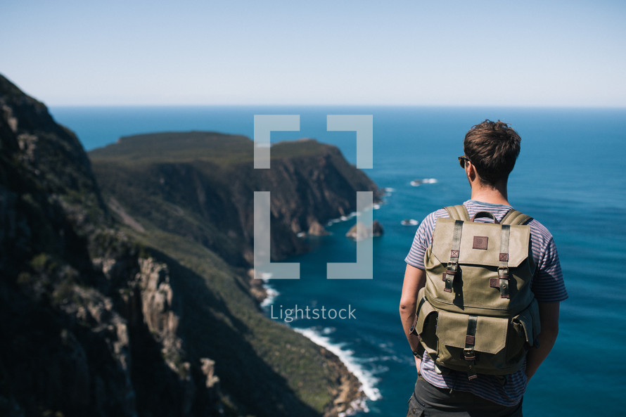 a man backpacking looking out a the view standing on cliffs in New Zealand 