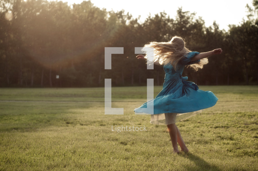 Girl twirling around outside in a field of grass.