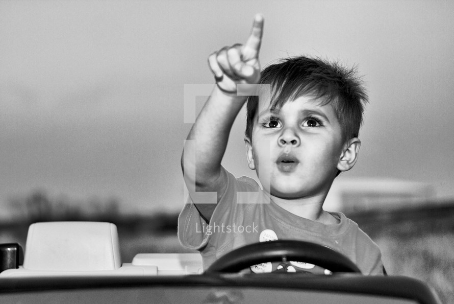 Boy in a toy car pointing at the sky