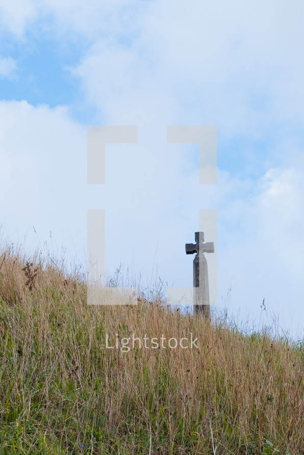 A cross in a field of grass against a blue sky.