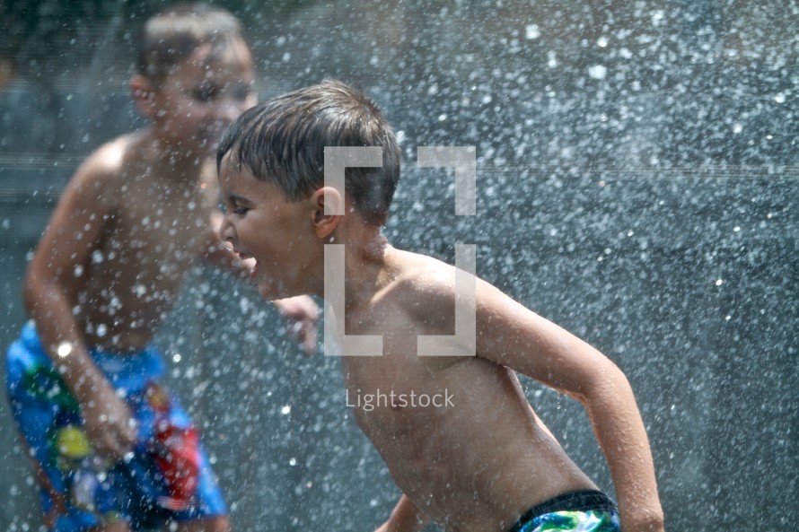 Two young boys playing in the sprinkler and getting sprayed with water