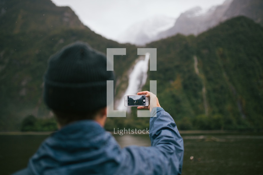 a man taking a picture of a waterfall in New Zealand 