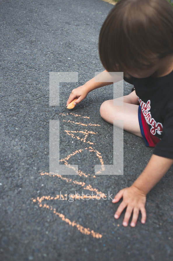 boy child writing his name with sidewalk chalk 