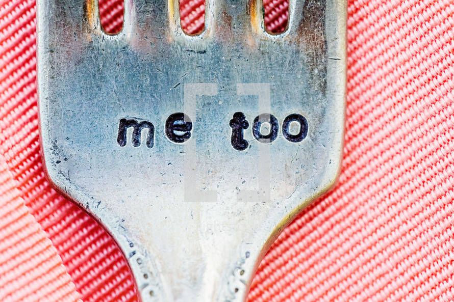 the words me too engraved stamped into a dinner fork sitting on a pink linen