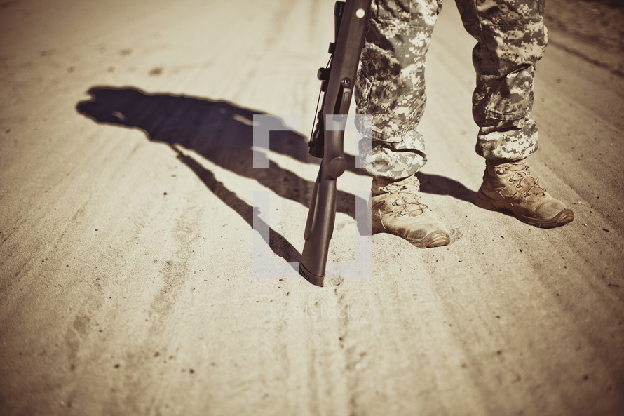 A soldier standing on a dirt road with a rifle.
