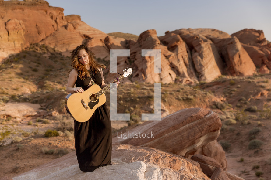 Woman with a guitar standing on a canyon ridge.