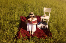 a woman reading a book on a blanket in the grass