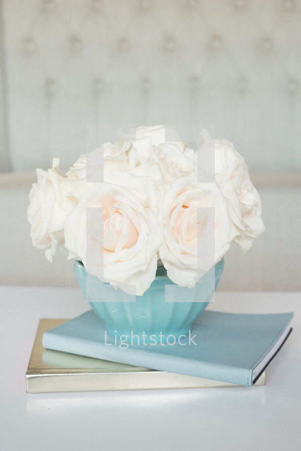 A blue vase of white roses on a stack of books.