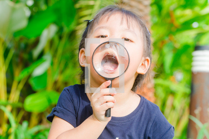 a little girl holding a magnifying glass over her mouth