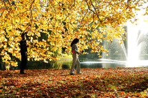woman walking under a fall tree and a fountain in a lake 