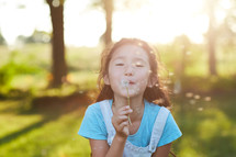 a girl blowing a dandelion 