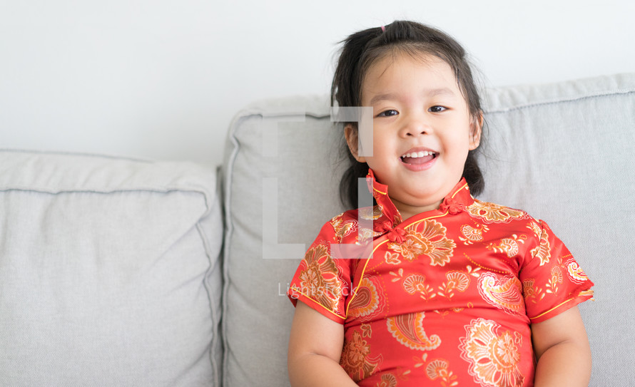 little girl in a traditional Chinese dress sitting on a couch 